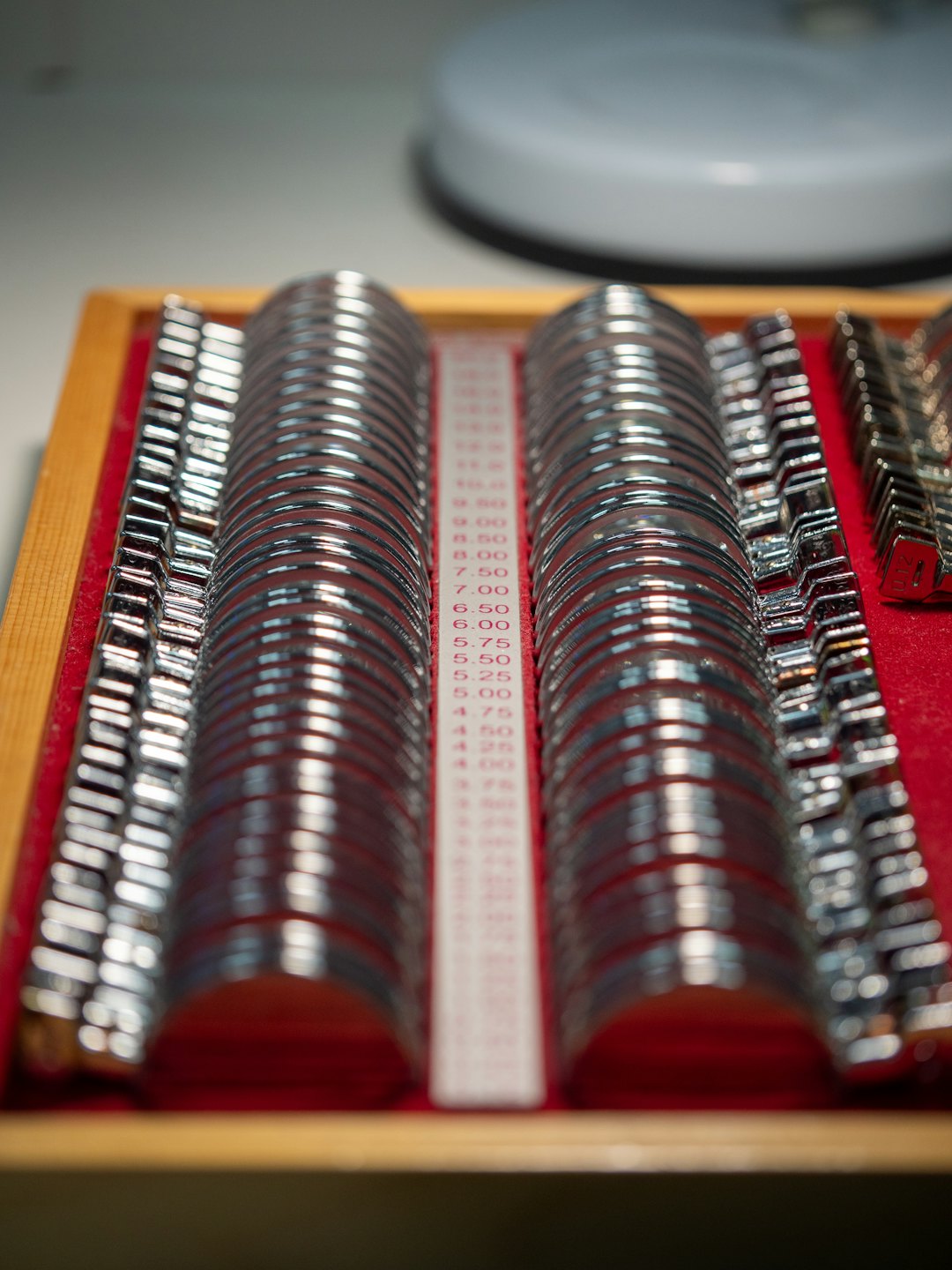 Silver trial lenses in a wooden box with numerical markings.